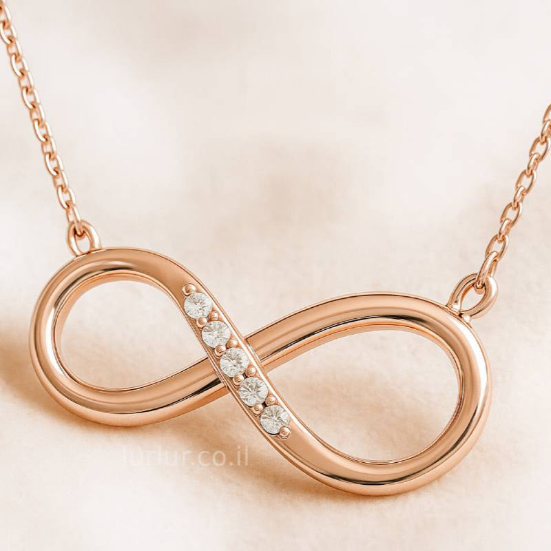Rose gold infinity necklace with small diamonds on a beige background