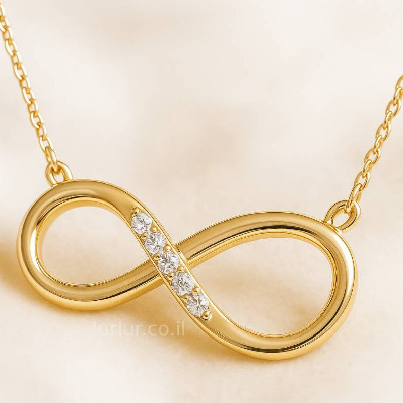 Gold infinity necklace with small diamonds on a beige background