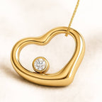 Gold heart-shaped pendant with a diamond on a beige background