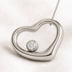 Heart-shaped silver pendant with a diamond on a light background
