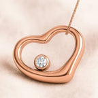 Rose gold heart-shaped pendant with a diamond on a beige background