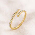 Gold open ring with diamond accents on a light pink background