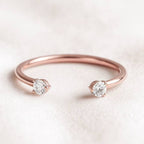 Rose gold ring with two diamonds on a light pink background