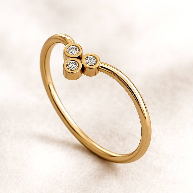 Gold ring with three diamond-like stones on a light beige background