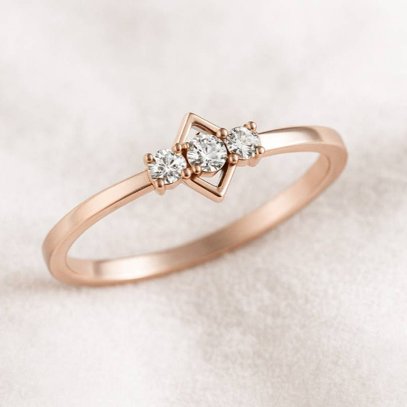 Rose gold ring with three diamonds on a light beige background