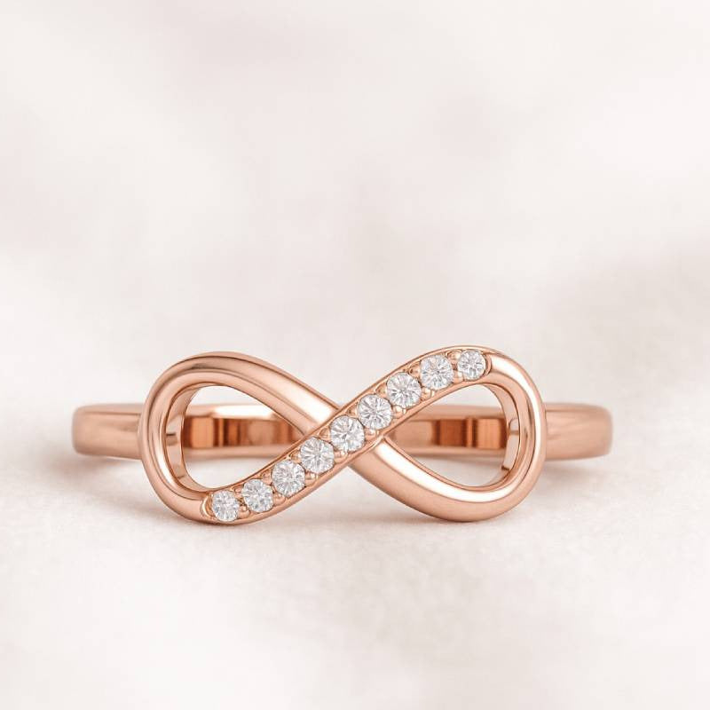 Rose gold infinity ring with diamonds on a light pink background