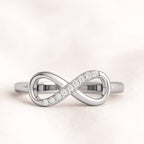 Gold infinity ring with small diamonds on a light pink background