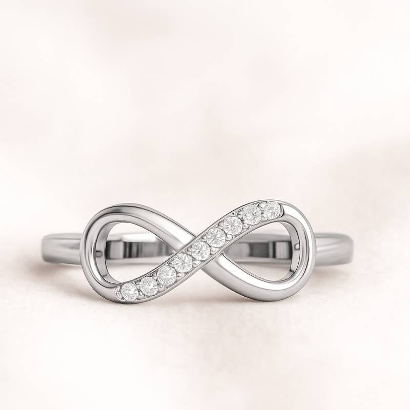 Gold infinity ring with small diamonds on a light pink background