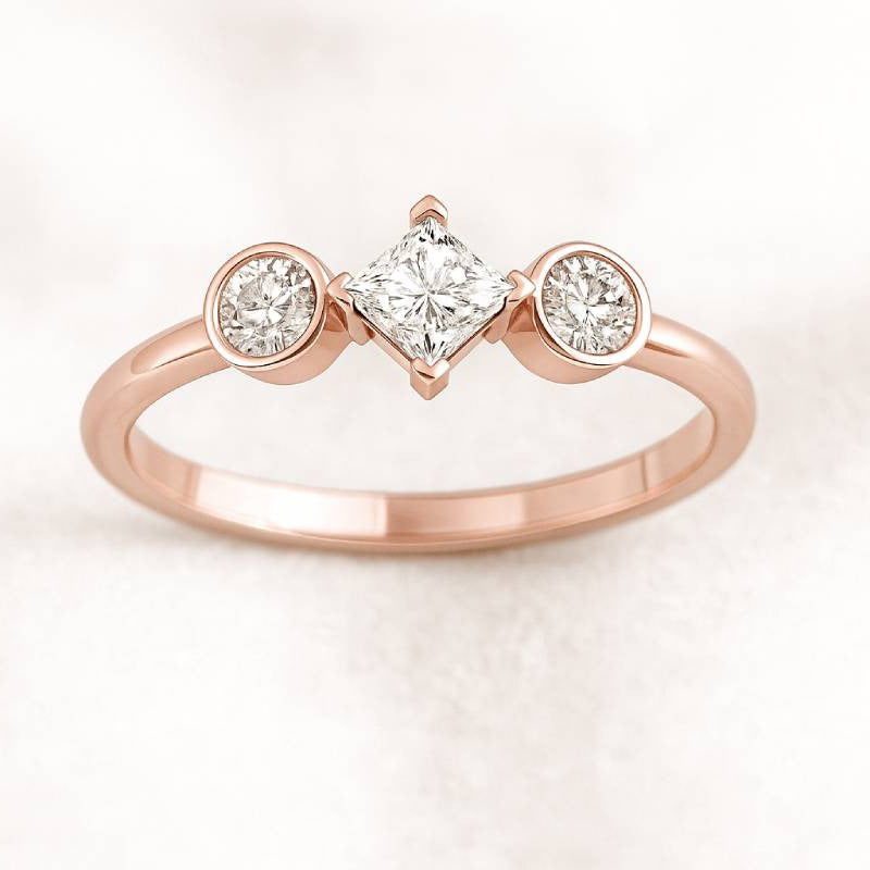 Rose gold ring with three diamonds on a light pink background