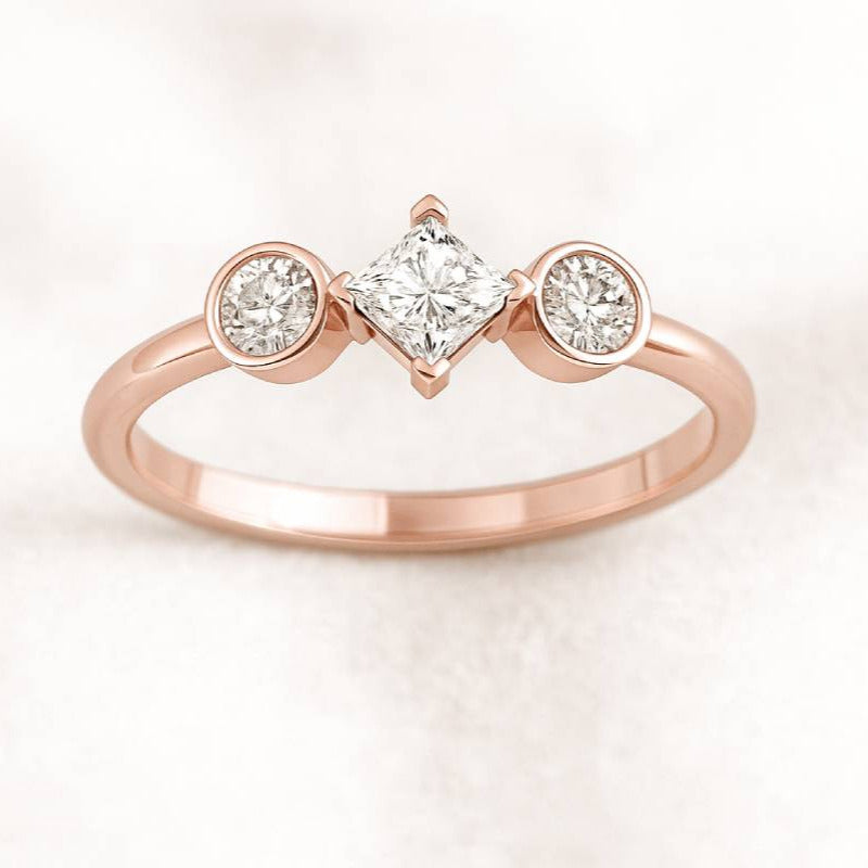 Rose gold ring with three diamonds on a light pink background