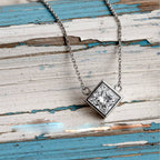 Gold necklace with a square-cut diamond pendant on a wood background