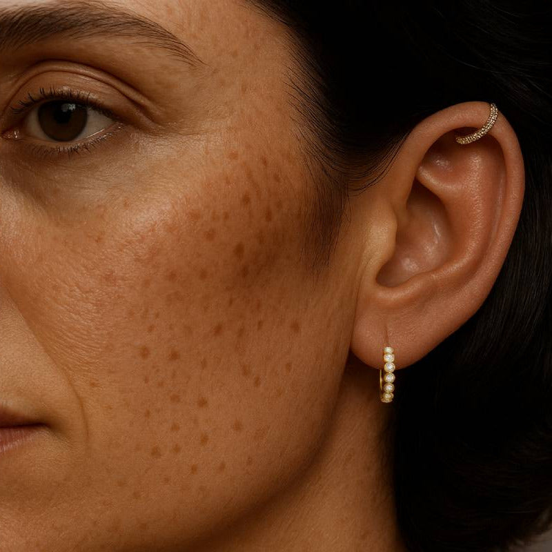 Close-up of a person wearing a gold hoop earring with a neutral background