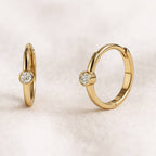 Gold hoop earrings with small round gemstones on a light beige background