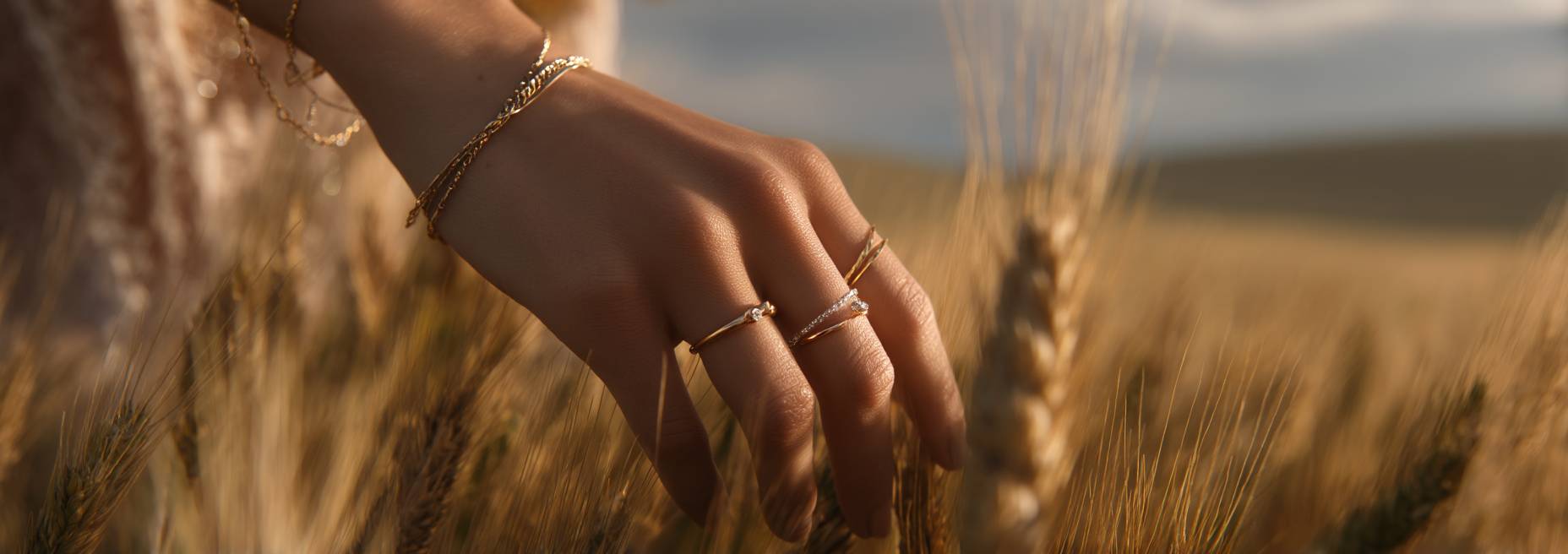 Hand with gold rings and bracelets touching wheat in a field