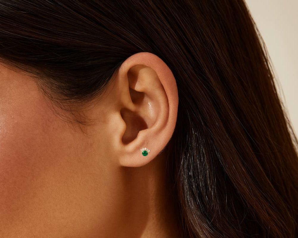 Close-up of an ear with a green gemstone earring against a blurred background