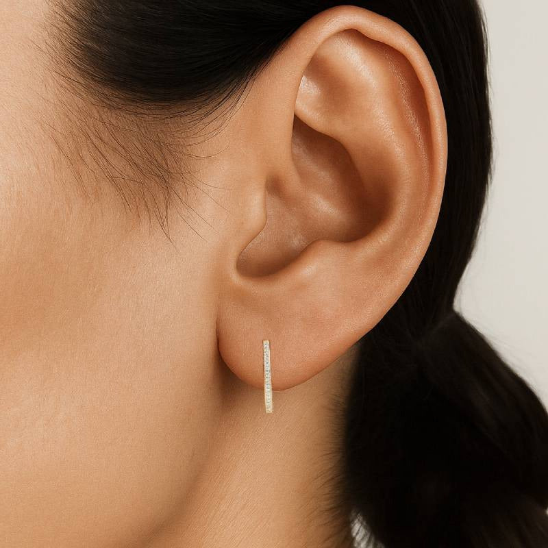 Close-up of an ear wearing a gold hoop earring on a neutral background