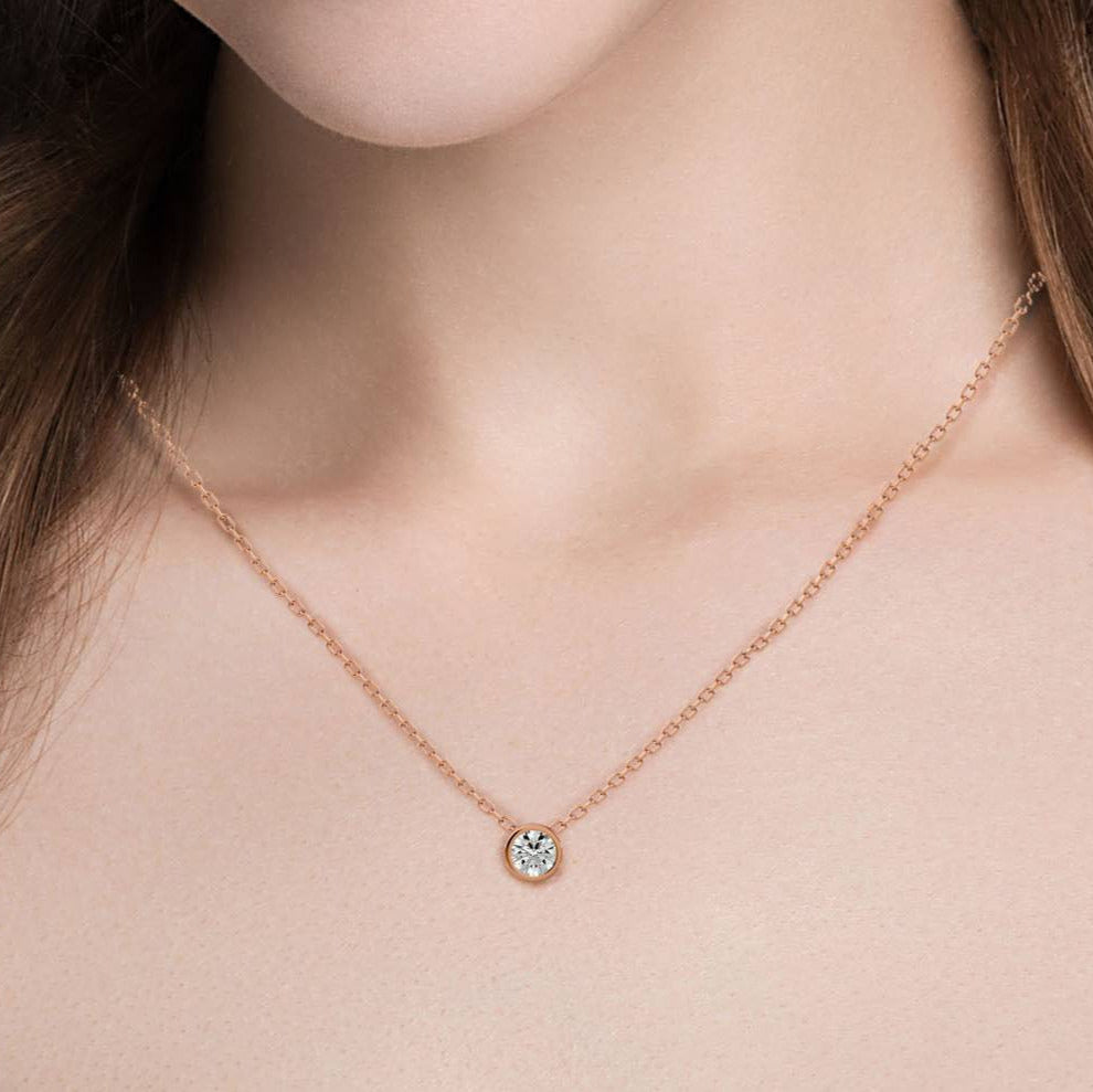 Rose gold necklace with a small round pendant on a person's neck